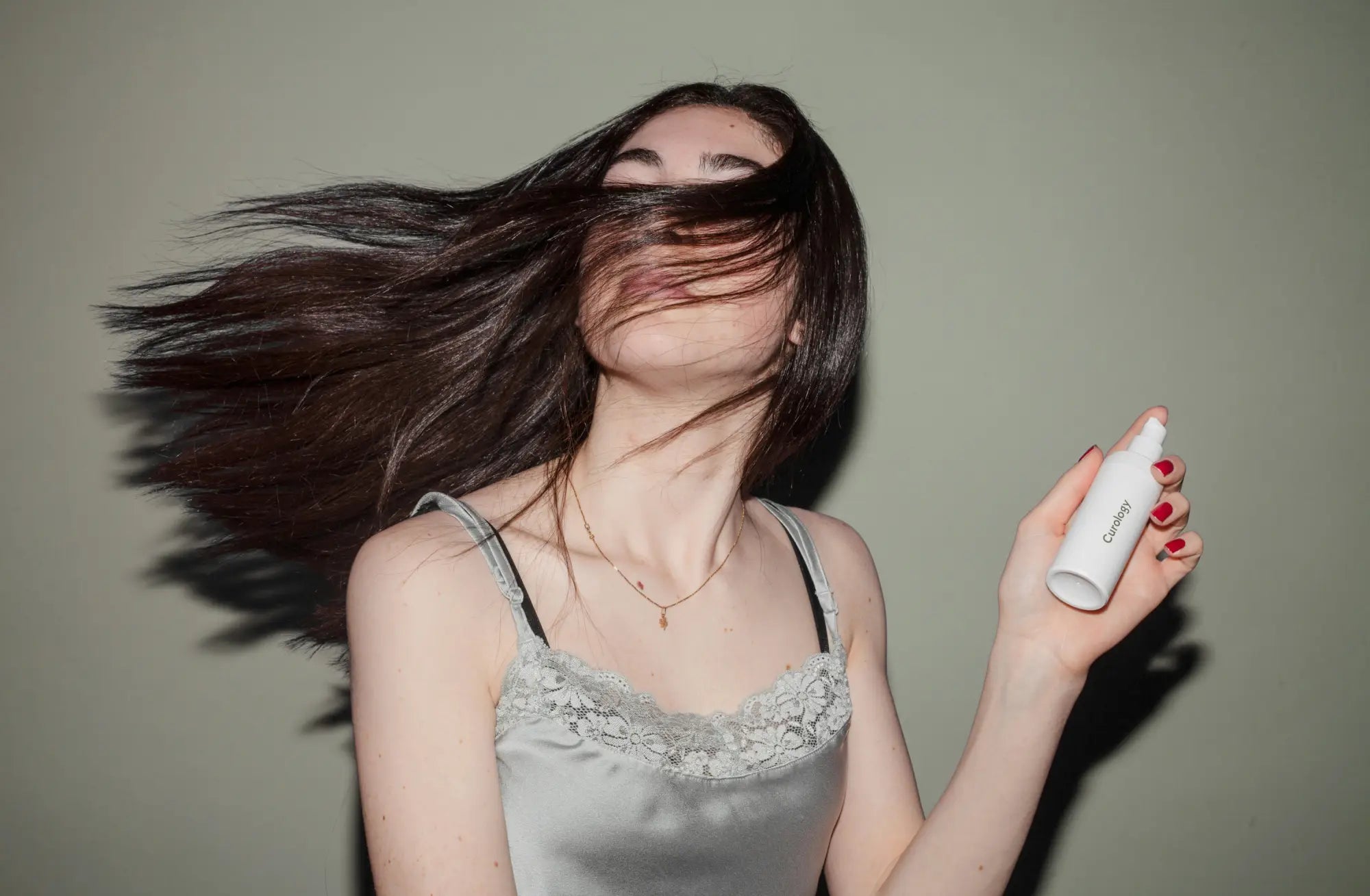 Woman with long dark hair flipping her head, holding a spray bottle for faster hair growth.