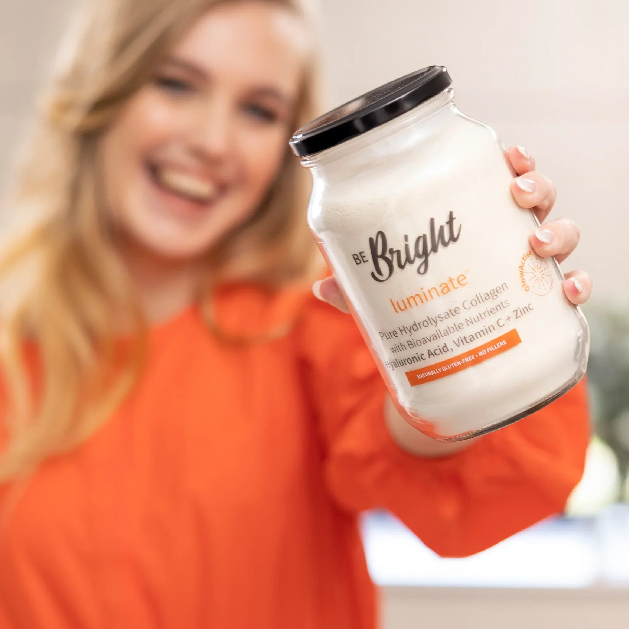 Be Bright Luminate Collagen Powder Jar 500g held by a smiling woman, showcasing radiant beauty and vitality.