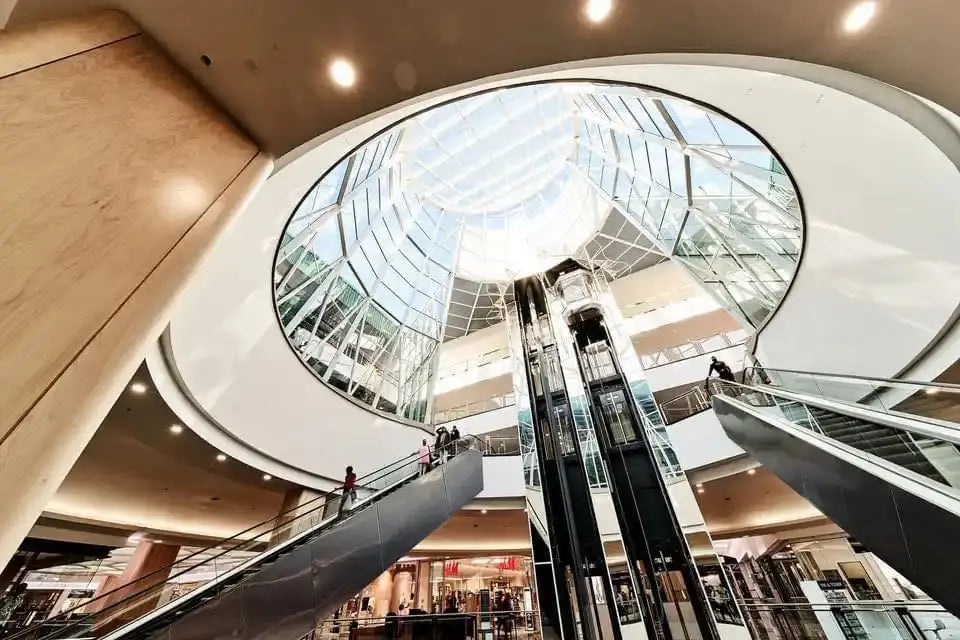 Glass-domed escalators with black handrails rising through a circular opening.