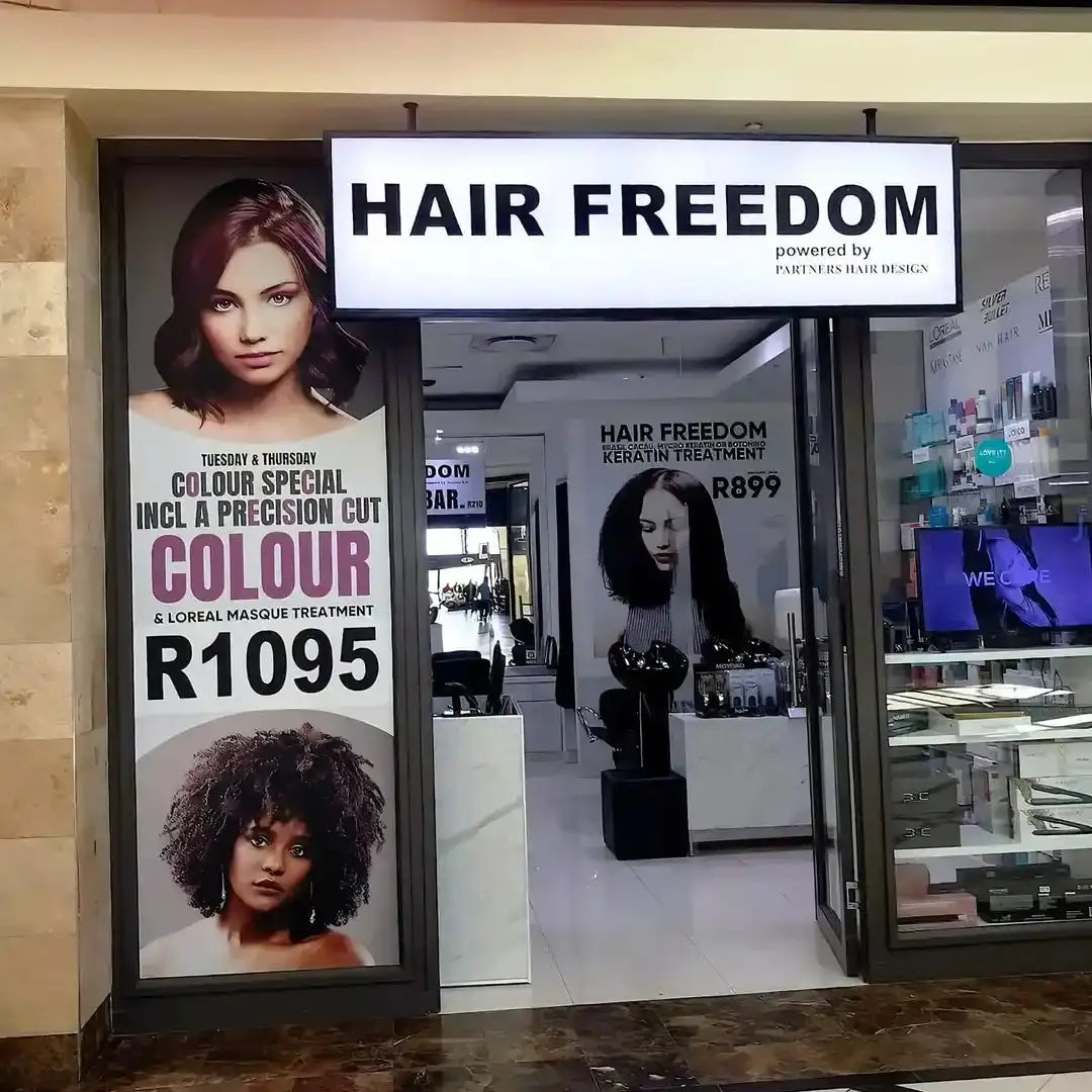 Hair salon storefront with ’Hair Freedom’ signage and promotional posters for hair coloring services.