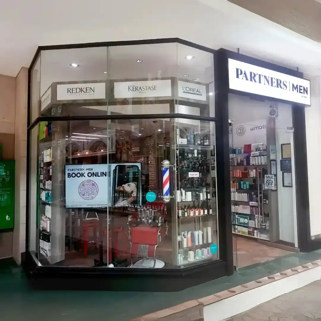Hair salon storefront with glass windows displaying Redken and Kerastase product displays.