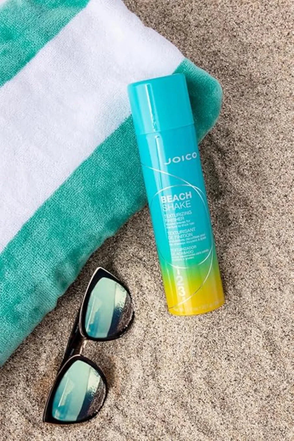 Joico Beach Shake: Beach Wave Spray for Effortless Texturizing. Teal and Yellow Hair Styling Product on Beach Towel and Sand.