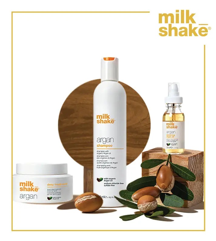 Milkshake Glistening Argan Oil Treatment bottle alongside argan shampoo and deep treatment with natural argan nuts and leaves