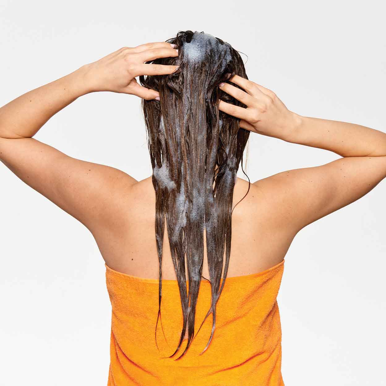 Woman with long hair washing with milkshake purifying blend shampoo lather in orange towel