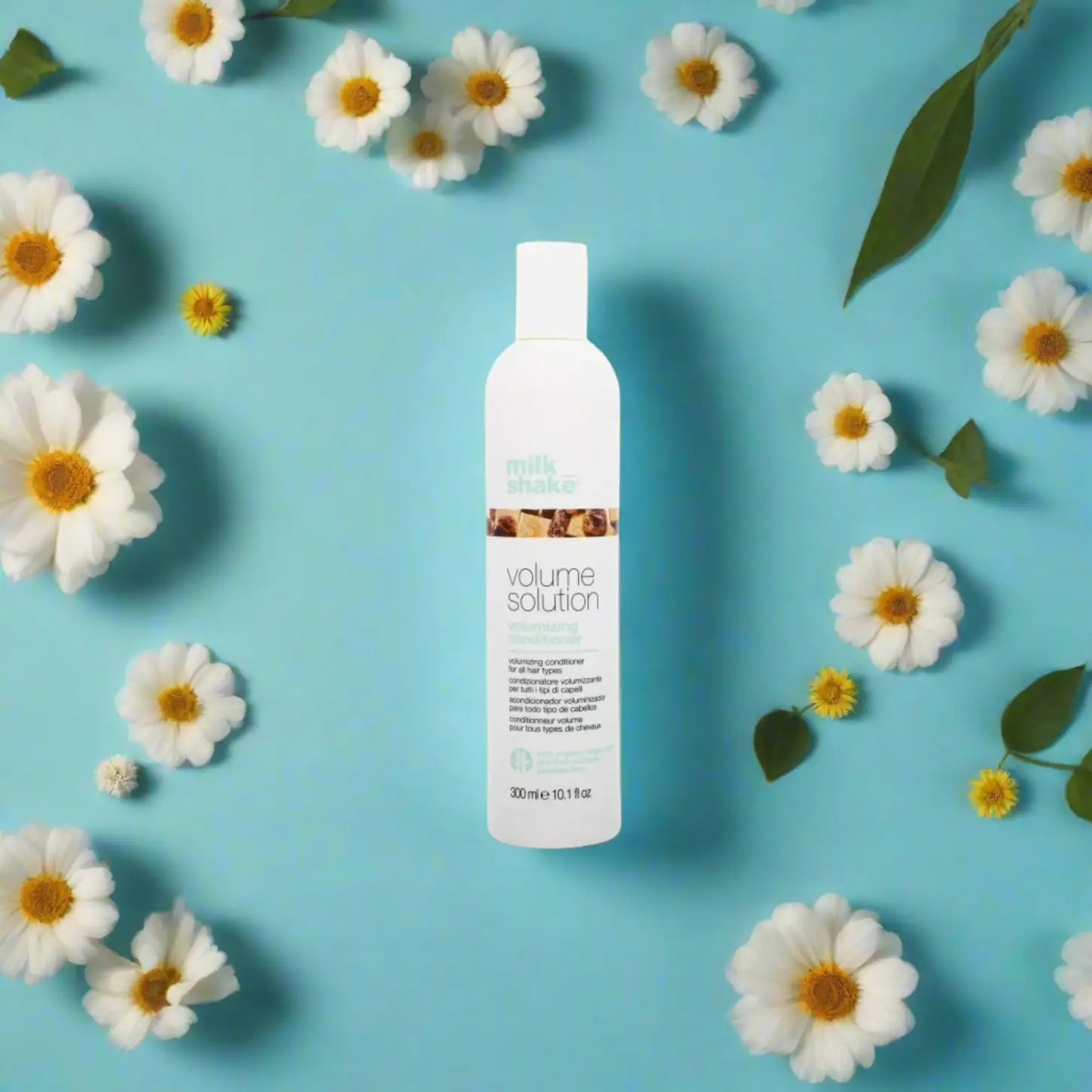 Milkshake Volume Solution Conditioner bottle surrounded by white daisies on a blue background