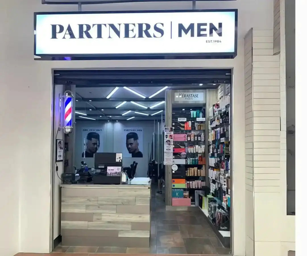 Modern men’s barbershop storefront with illuminated signage and traditional barber pole.