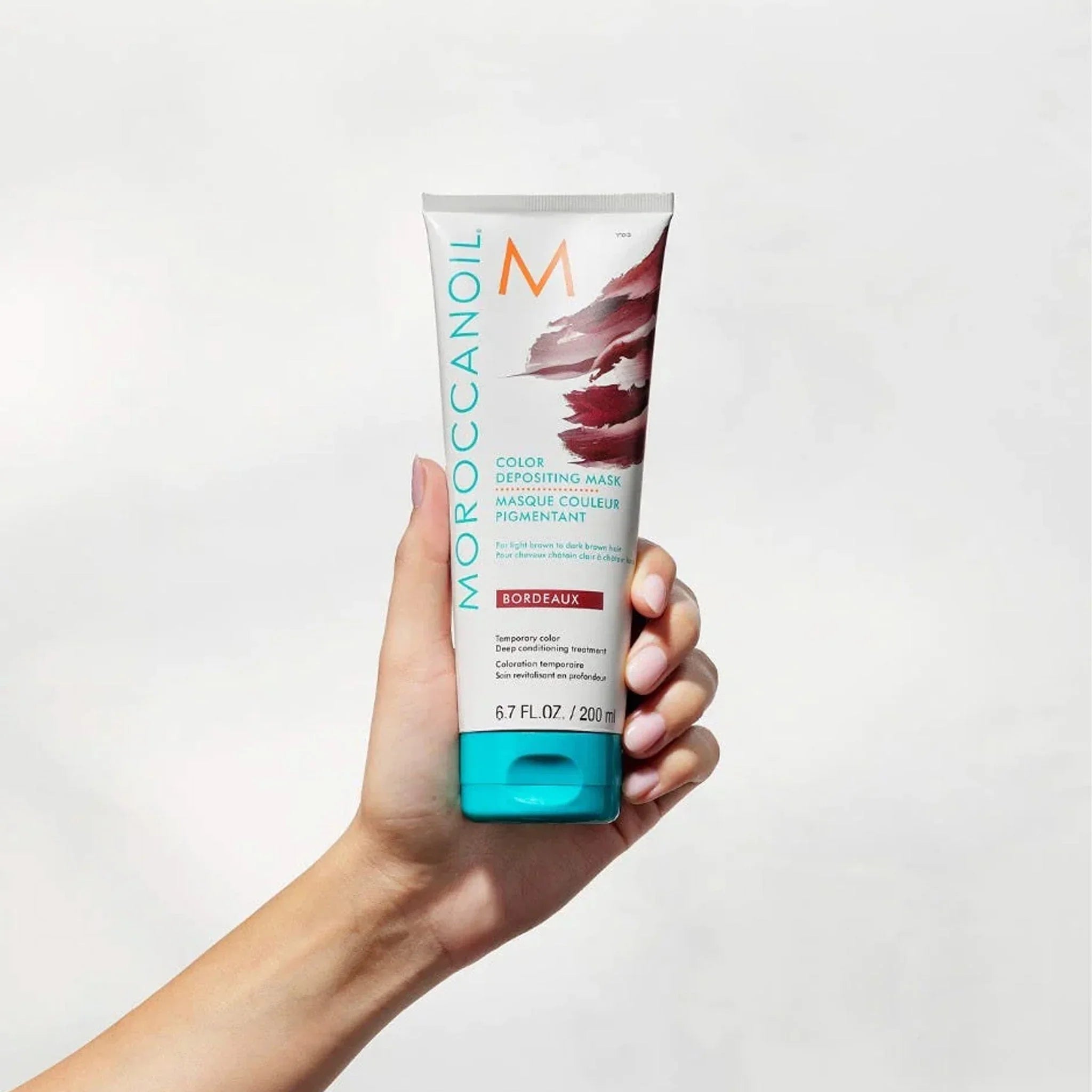 Hand holding Moroccanoil Color Deposit Mask Bordeaux 200ml for vibrant hair color