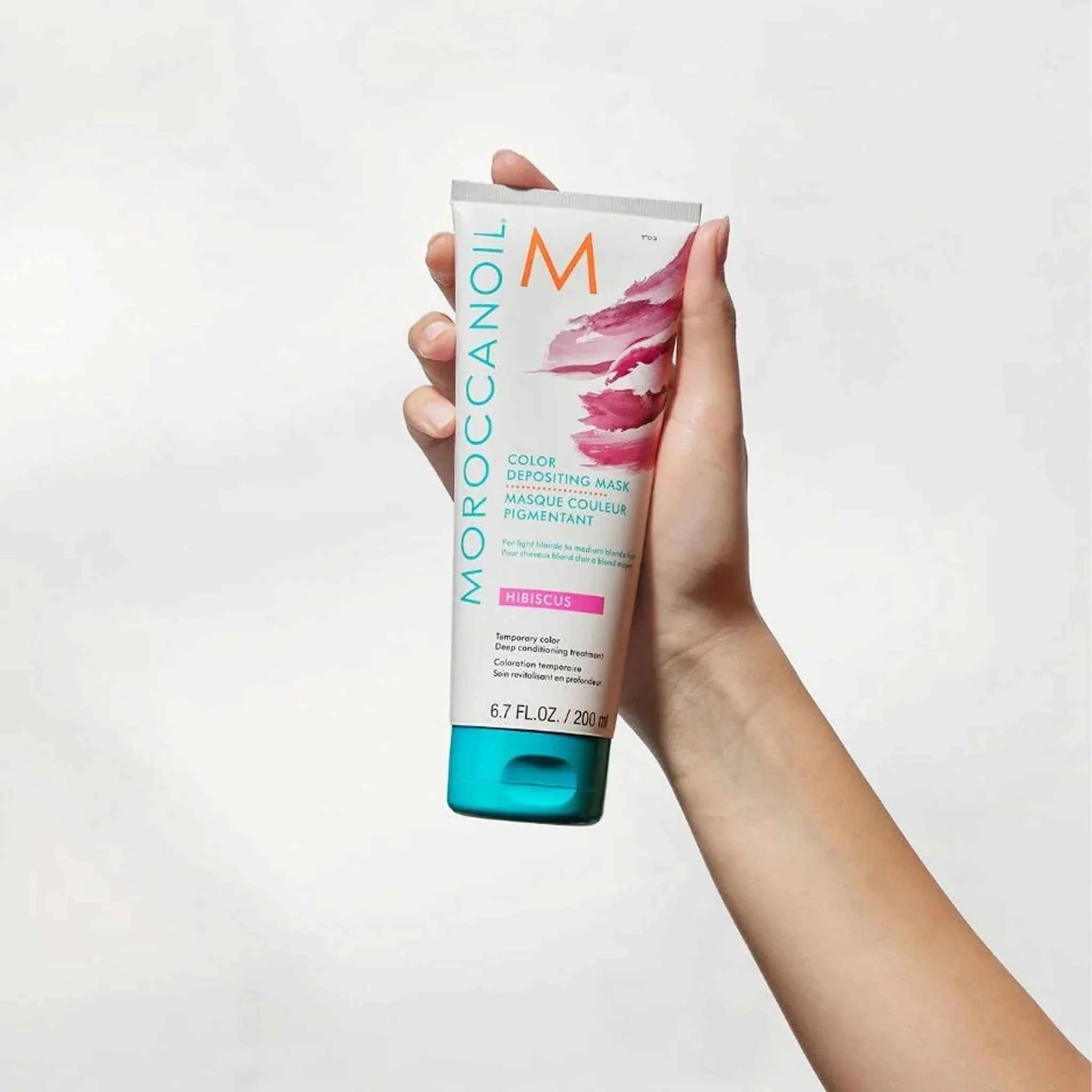 Hand holding Moroccanoil Color Deposit Mask Hibiscus tube hair treatment product with pink and turquoise design