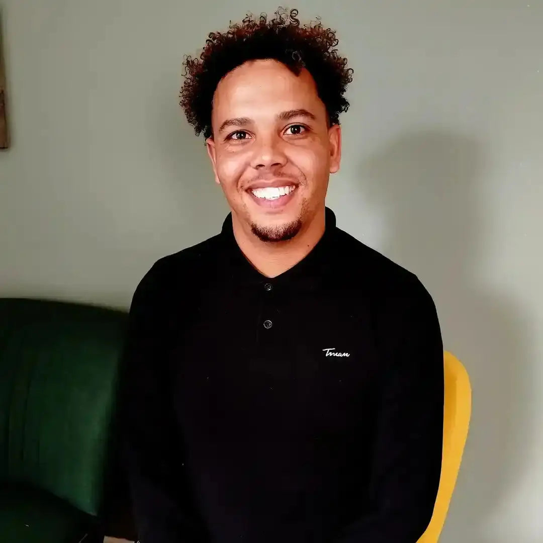 A person wearing a black polo shirt with curly hair and a bright smile.