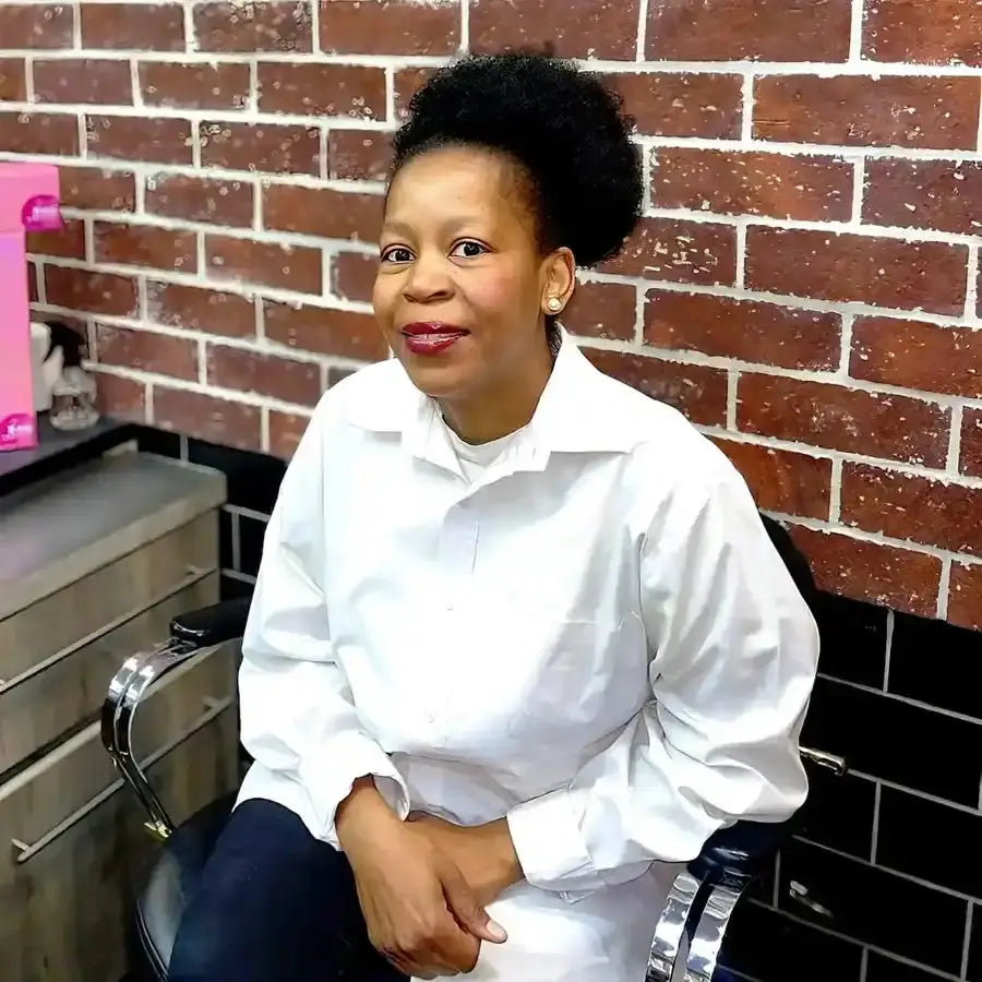 A person wearing a crisp white button-down shirt and dark pants sits casually against a brick wall.