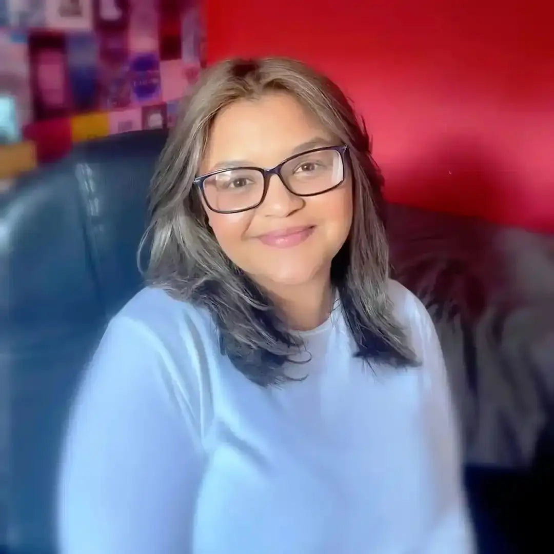 A person wearing glasses and a light blue sweater with gray hair smiling at the camera.