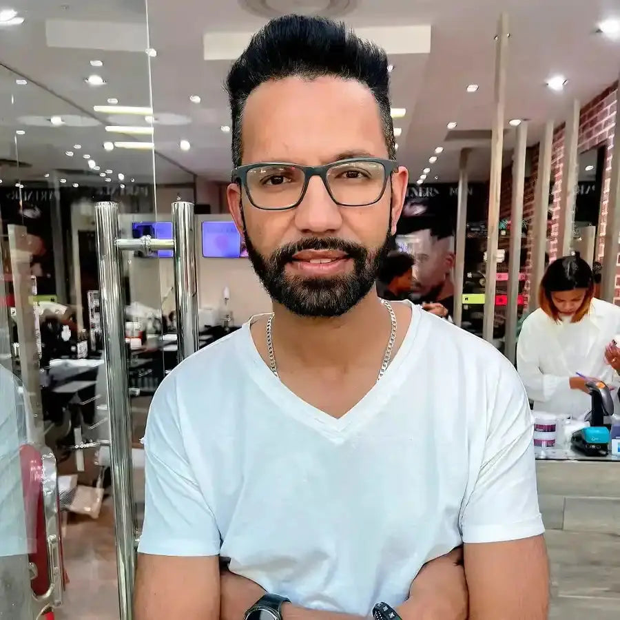 A person wearing glasses and a white v-neck t-shirt with a silver necklace.