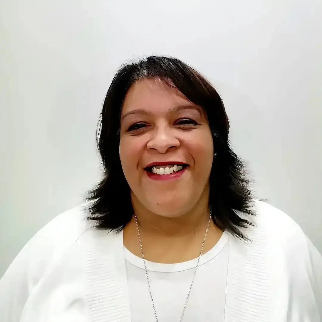 A smiling person wearing a white sweater and necklace.