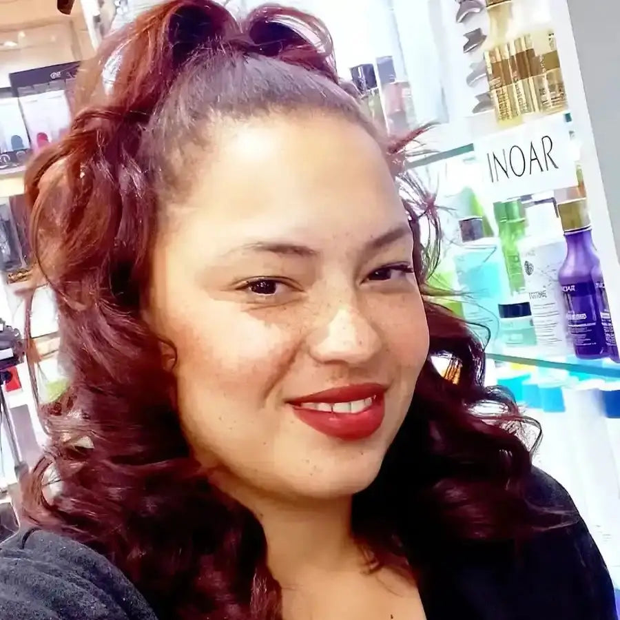 A selfie showing burgundy curled hair, red lipstick, and a warm smile.