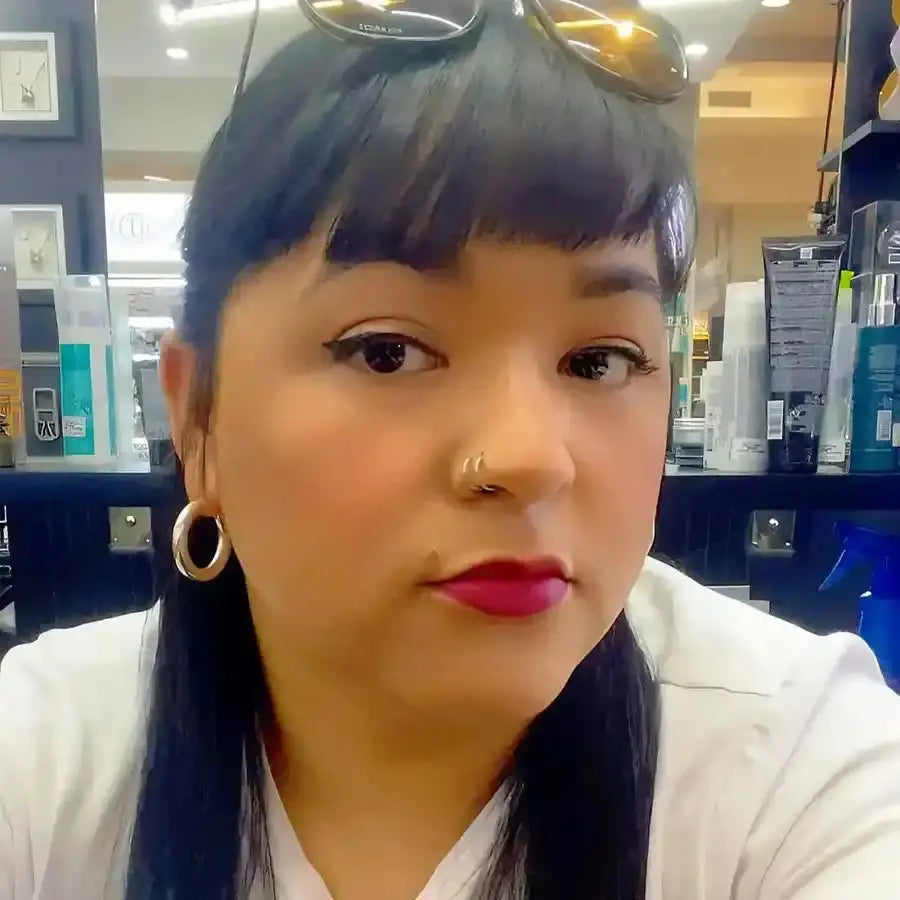 A selfie showing someone wearing a white top, red lipstick, gold hoop earrings, and sunglasses positioned on top of their dark hair.