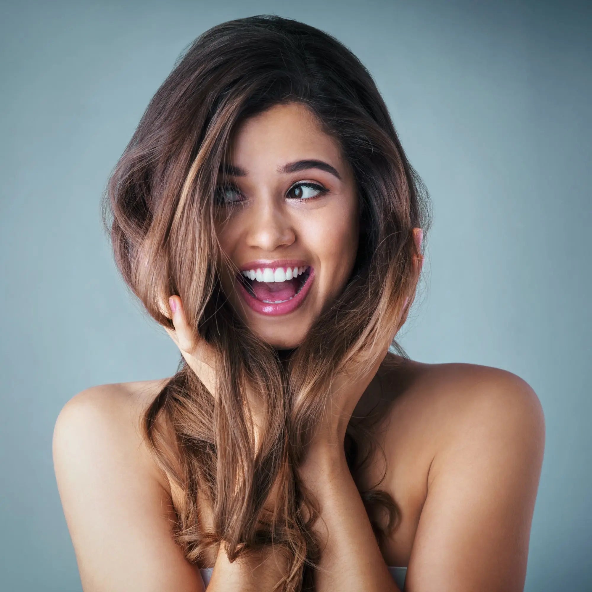 Smiling woman with long wavy ombre hair and pink lipstick showcasing Partners Hair Design.