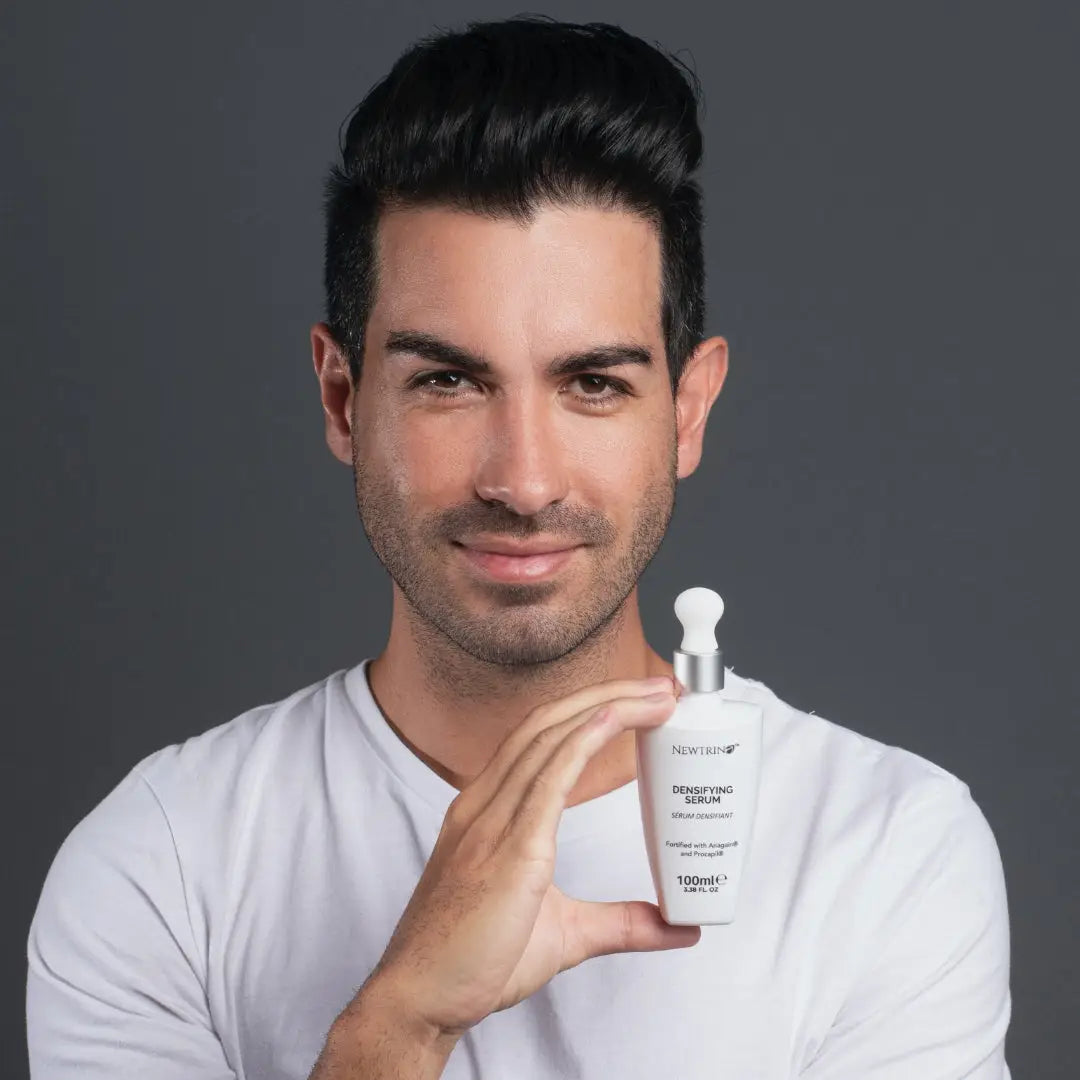 White bottle of hair growth serum held by man in shirt, showcasing active ingredients.