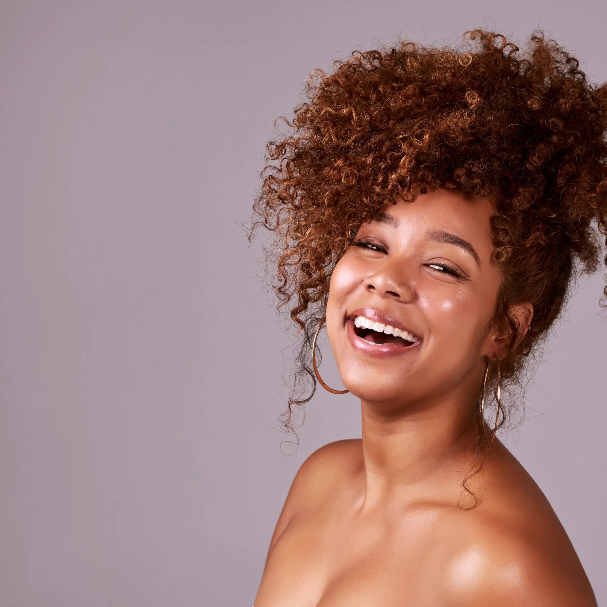 Joyful woman with curly hair laughing, showcasing healthy hair growth and springy curls.