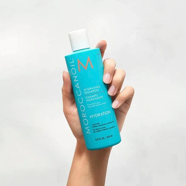 Turquoise bottle of Moroccanoil Curl Enhancing Shampoo held in a hand for shine and energy.