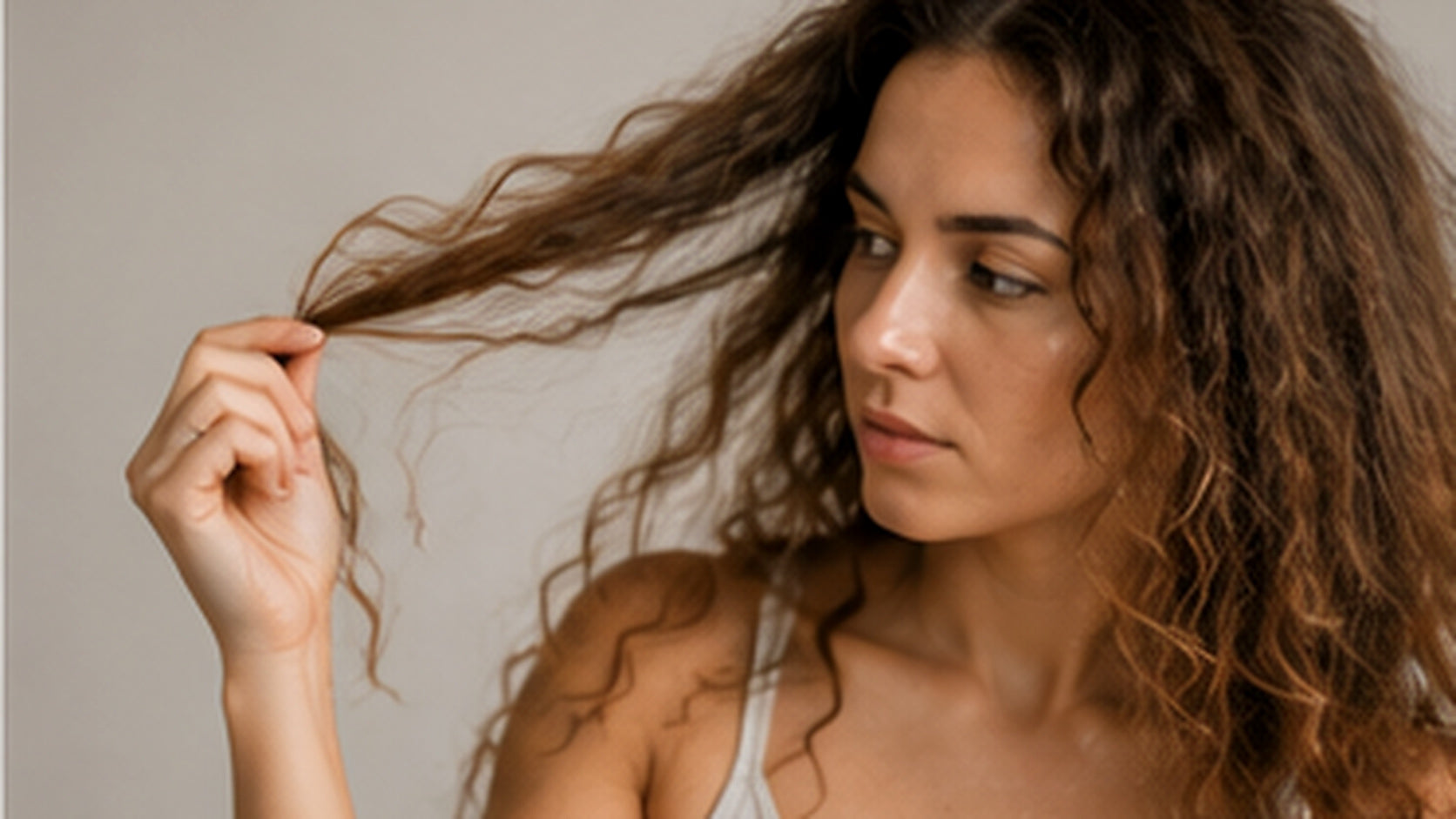 Woman examining dry frizzy curls in soft natural light