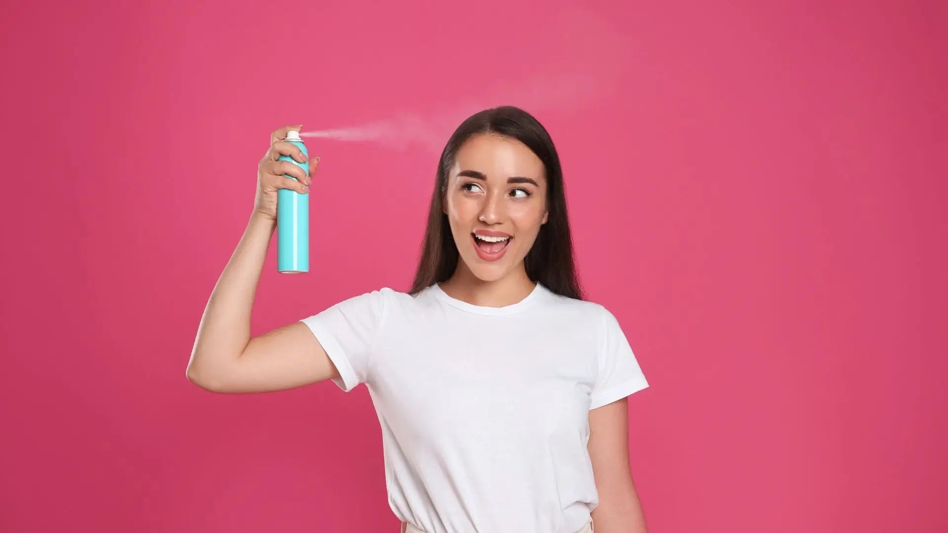 Smiling woman in a white t-shirt holding dry shampoo to combat excess oil in dark hair