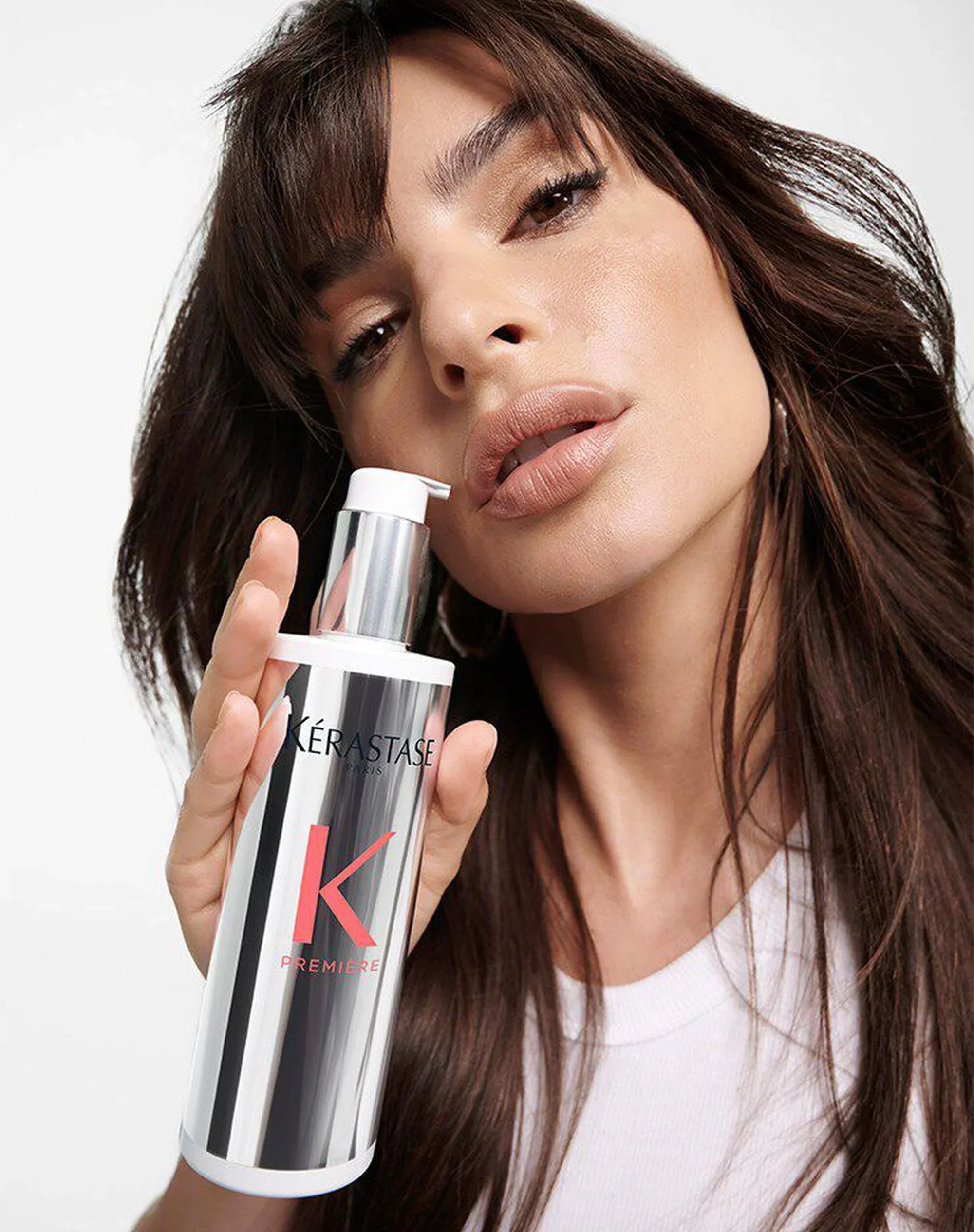 Woman with long dark hair holds a metallic bottle of Kerastase Elixir Ultime.