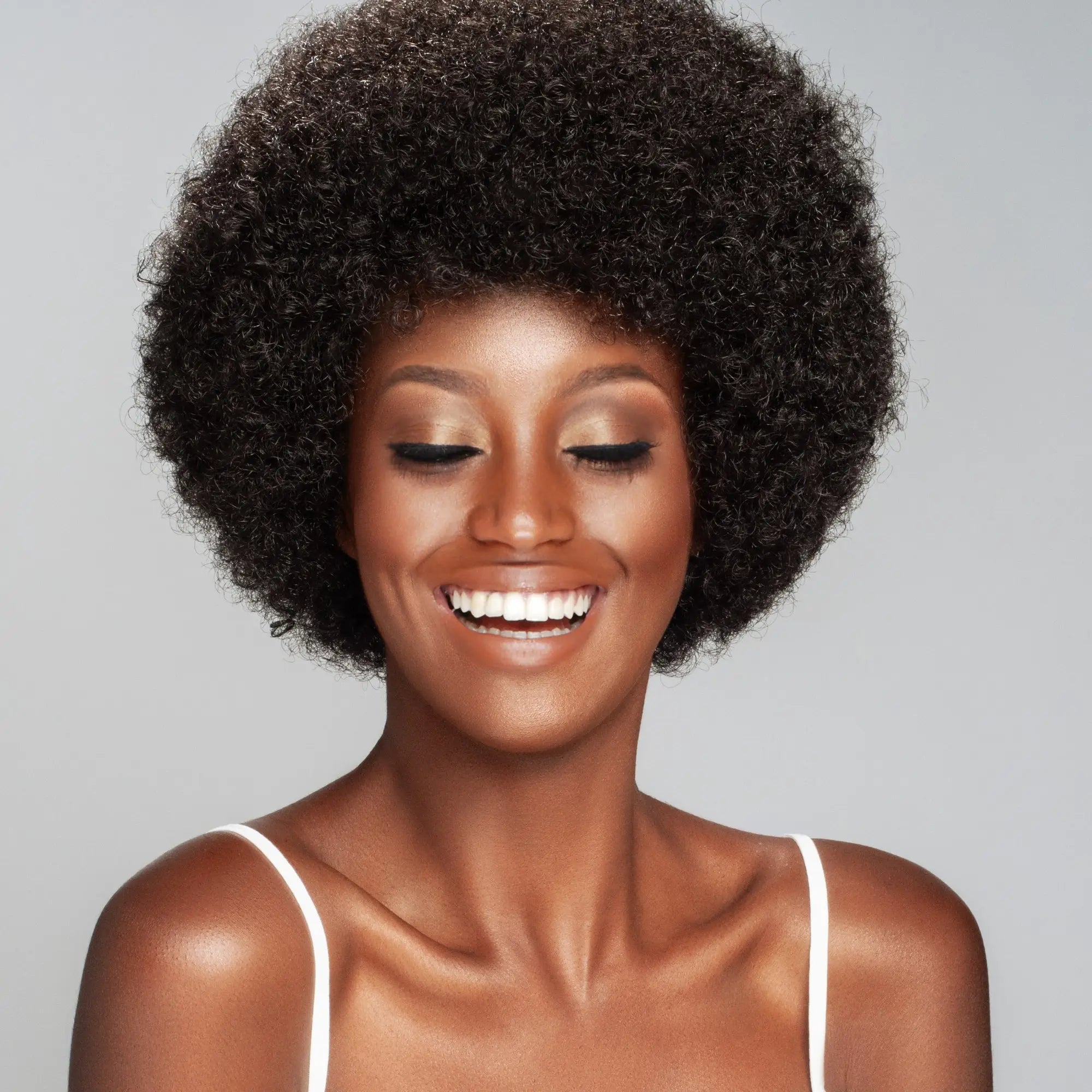 Smiling person with afro hairstyle and glowing makeup using sulphate-free shampoos in South Africa