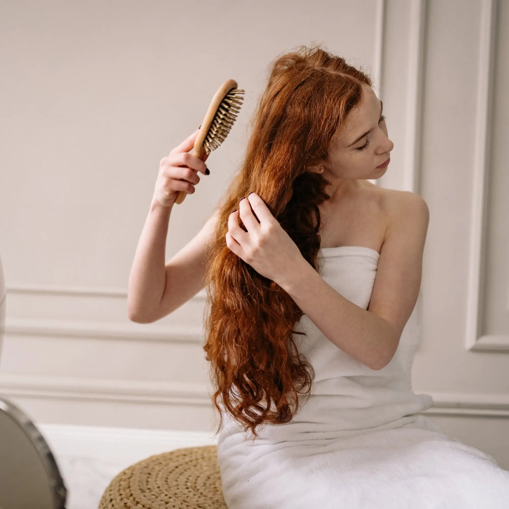 Woman with long wavy red hair brushing in a towel, ideal for heat protect spray usage.