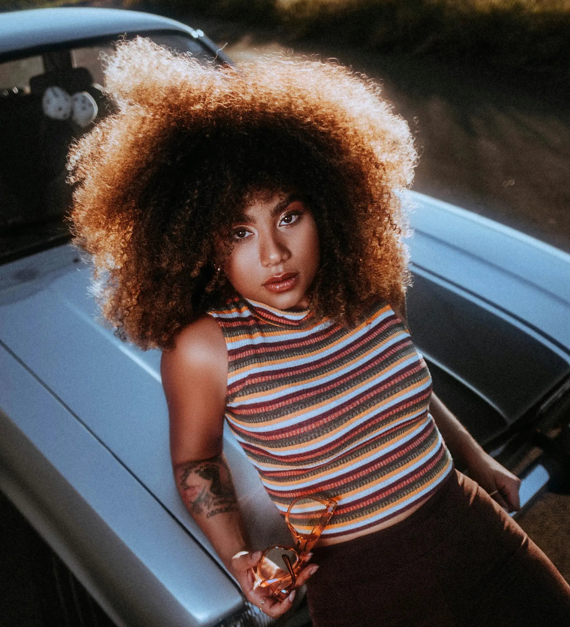 Woman with voluminous curly hair in a striped sleeveless top embracing her natural curl pattern.