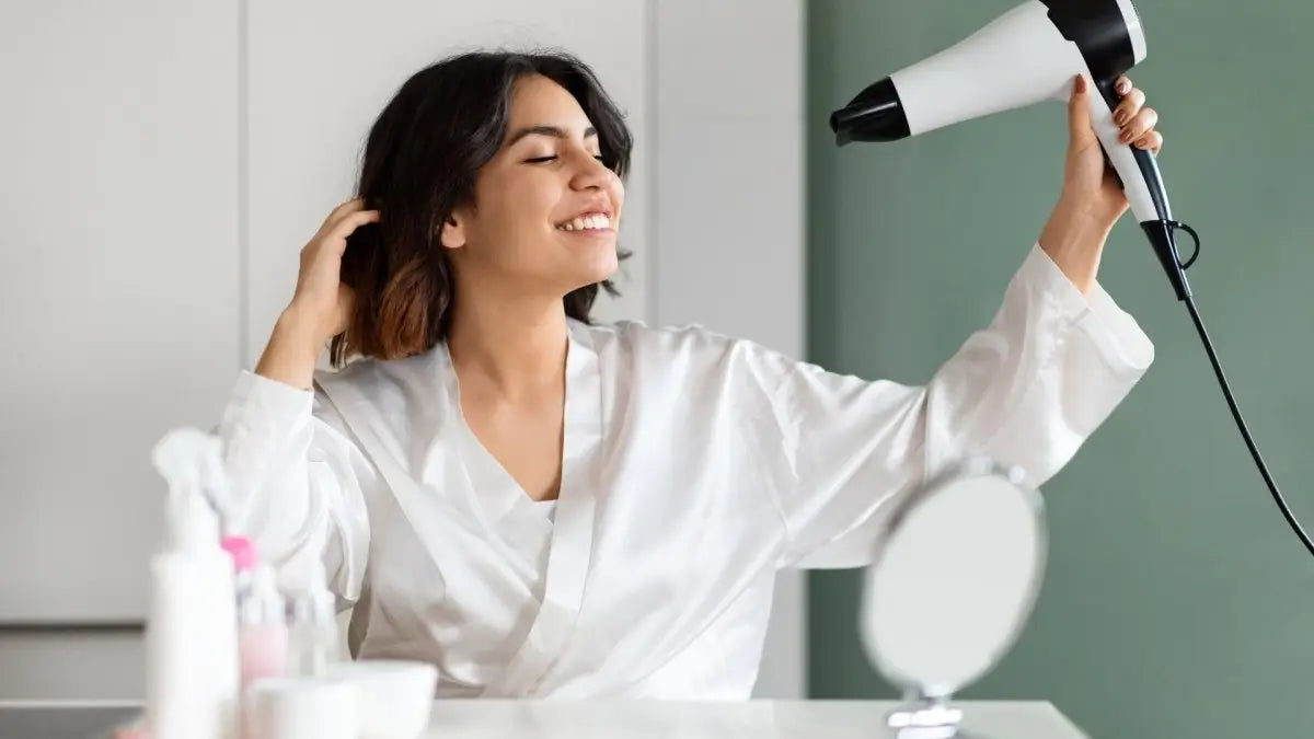 Woman in a white bathrobe using a Moyoko E8 hairdryer to avoid heat damage.