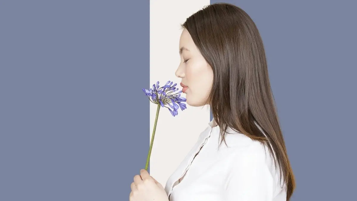 Woman with long dark hair enjoying the scent of a purple flower for Flower Fragrance Shampoo.