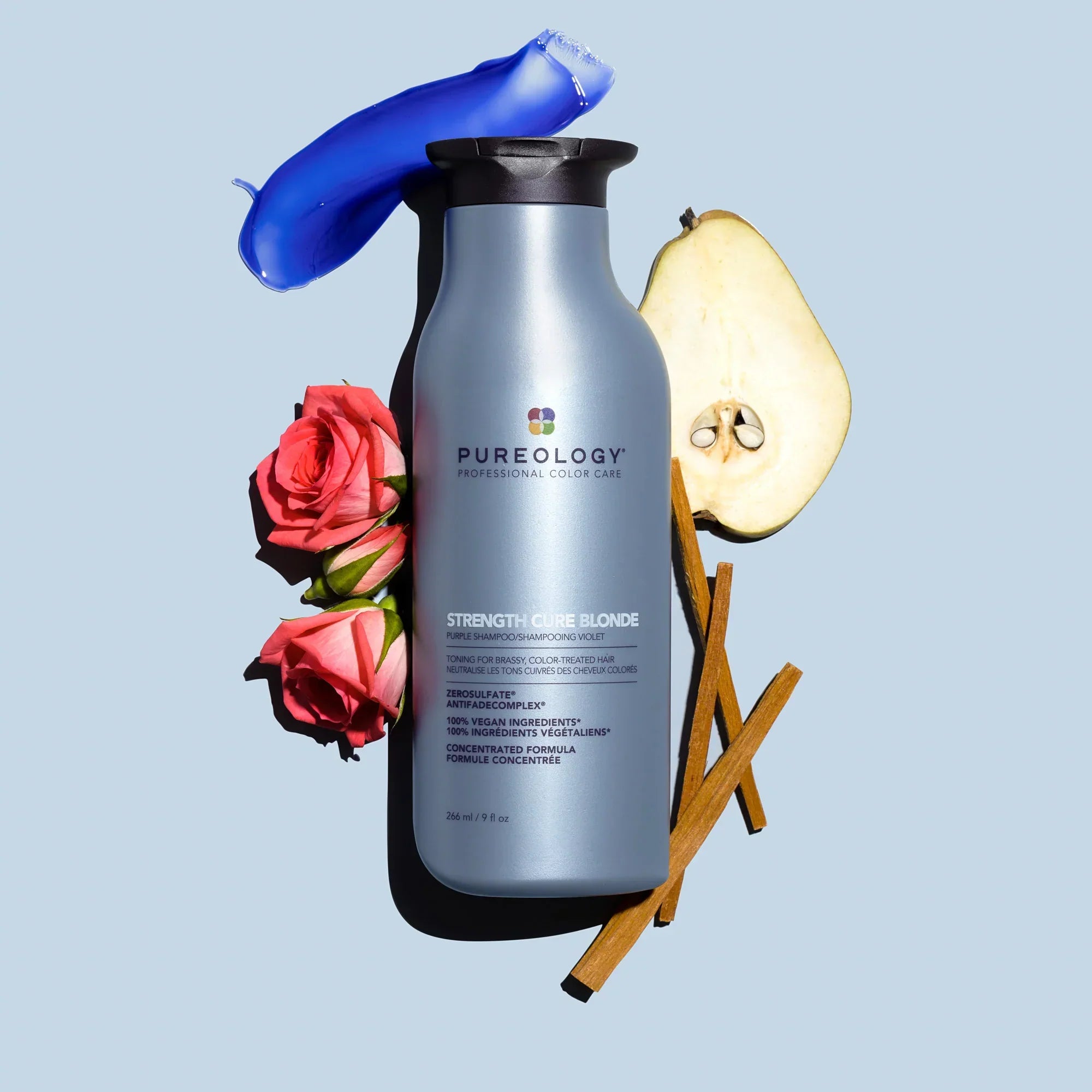 Silver Pureology hair care product surrounded by roses, pear, and cinnamon sticks.