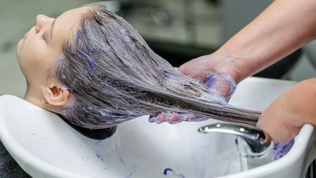 Hair being dyed purple and washed in a salon sink, highlighting purple shampoo benefits.