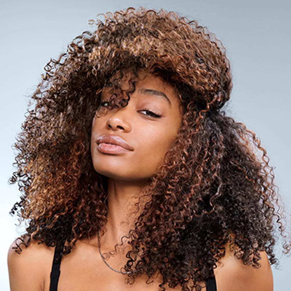 Voluminous curly brown hair enhances a warm complexion, showcasing Redken Extreme products.