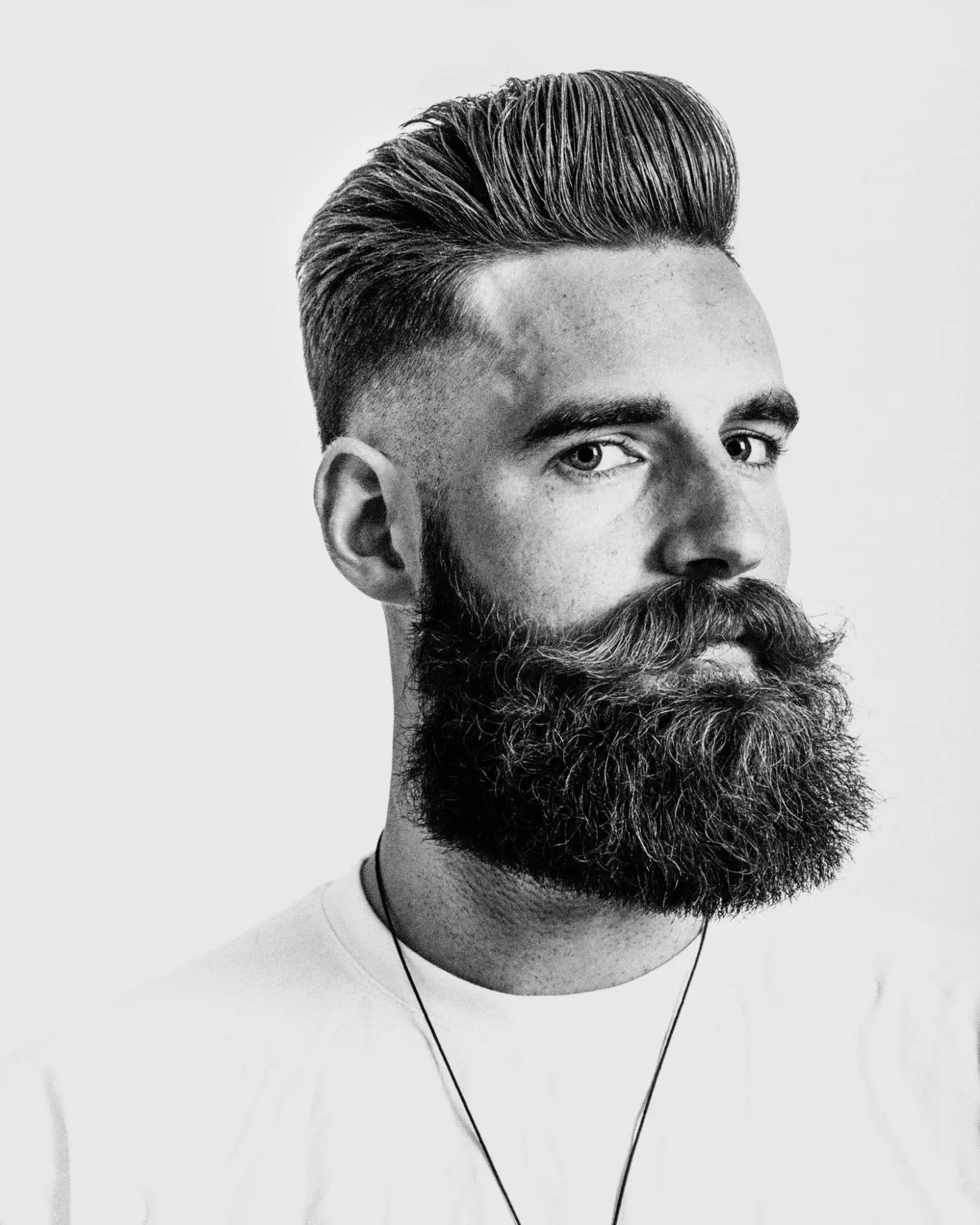 Black and white portrait of a man showcasing iconic hair and beard with grooming products.