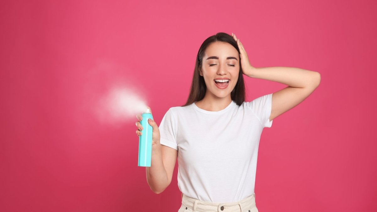 Woman in a white t-shirt laughing while holding dry hair shampoo spray bottle.