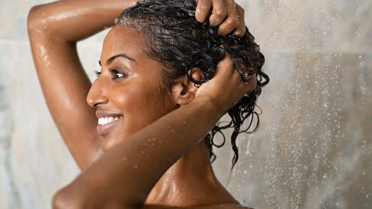 Smiling woman with wet curly hair using Kerastase Bain Satin Riche while styling her hair