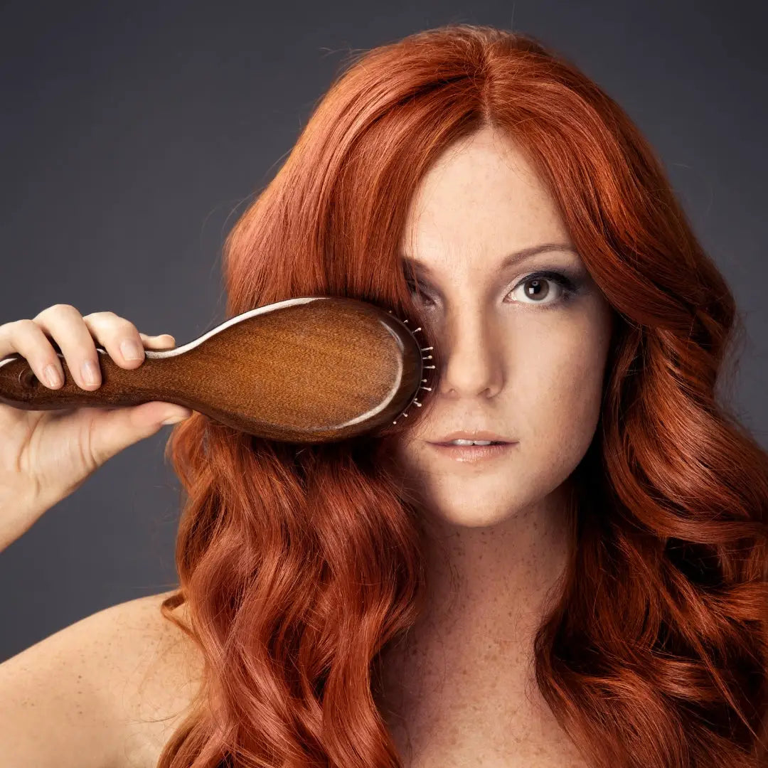 Woman with vibrant red hair showcasing Hailo detangling brush over one eye.