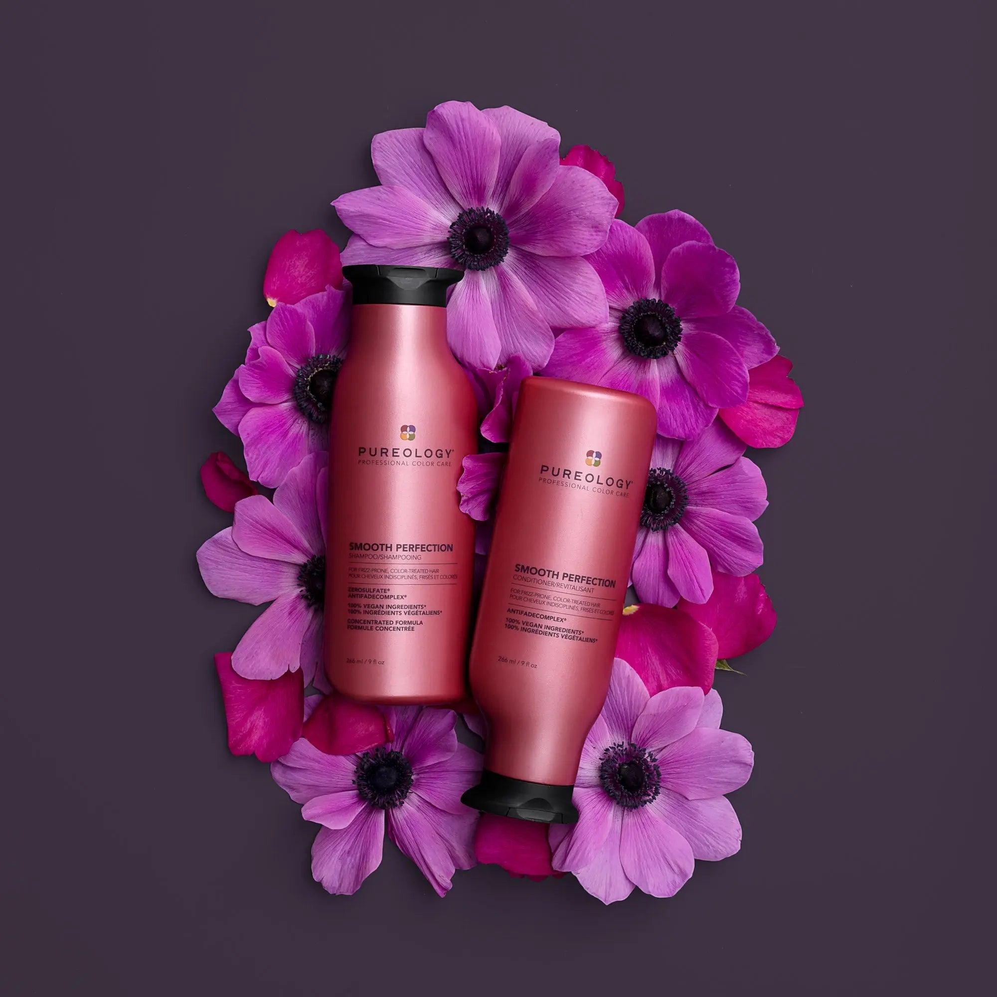 Two pink hair conditioner color bottles amidst vibrant purple flowers.