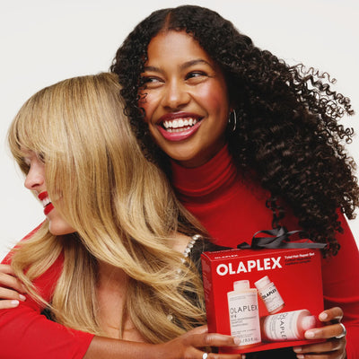 Two smiling women with healthy hair holding the Olaplex Total Hair Repair Set gift box