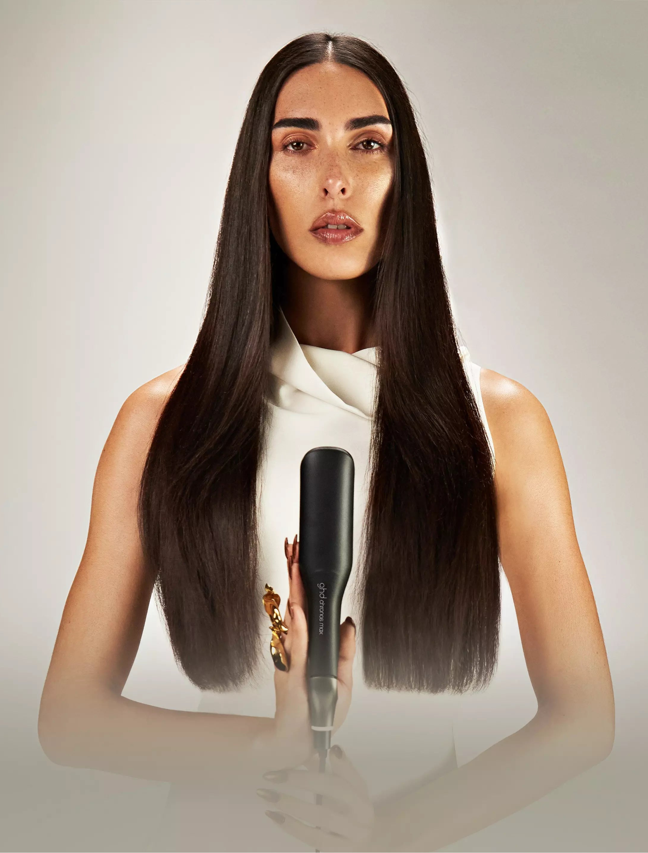 Woman holding a hair straightener with a neutral background