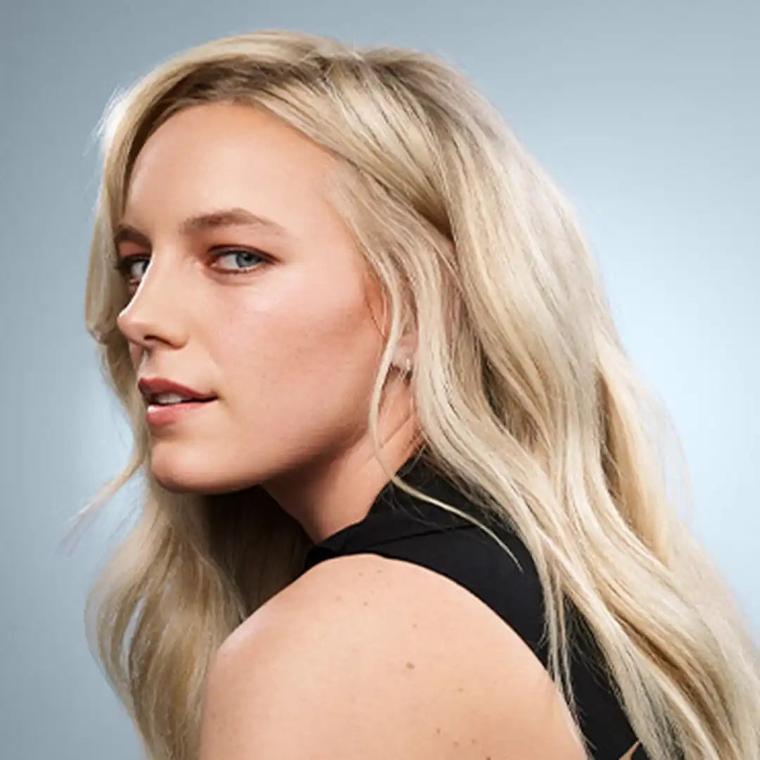 Blonde woman with long wavy hair wearing a black top, looking over her shoulder.