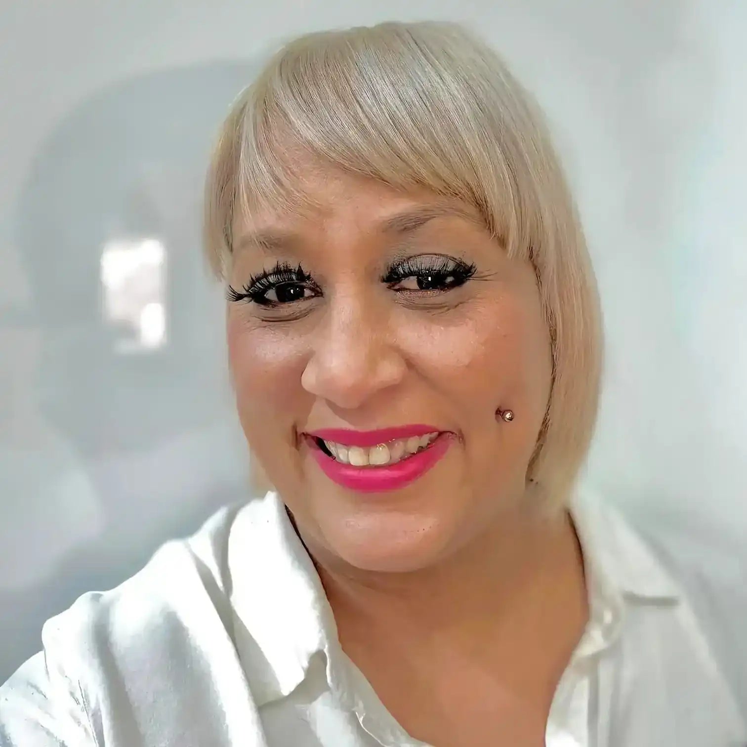 A close-up selfie showing bright pink lipstick, dramatic eye makeup, and platinum blonde hair with bangs.