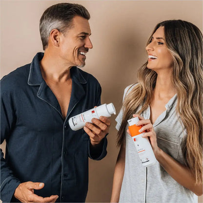 Smiling couple holding skincare or beauty product bottles while looking at each other.