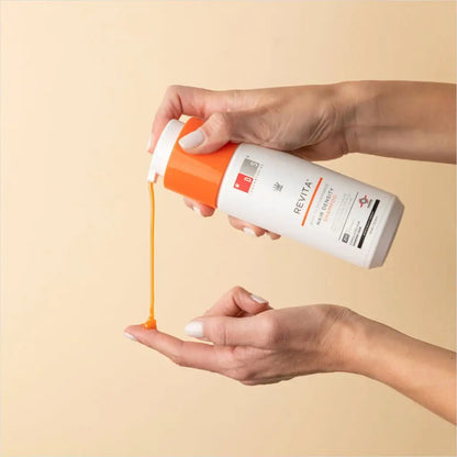 Bottle of orange-colored skincare product being squeezed to dispense liquid into a hand.