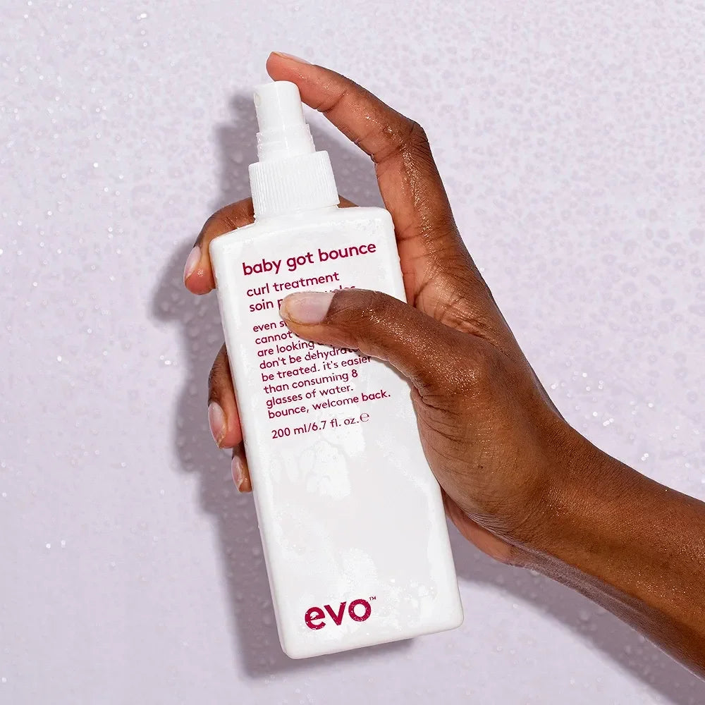 Hand holding a white bottle of EVO Baby Got Bounce Curl Treatment styling aid with red text