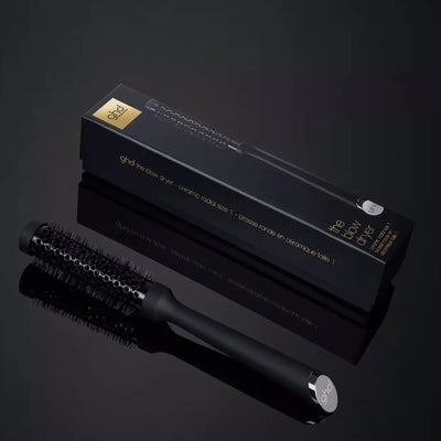 GHD brush: Blow dry brush for volume. GHD ceramic radial brush size 1 (25mm barrel) and packaging on black reflective surface.