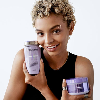 Woman with short curly blonde hair holding Kerastase Blond Absolu Bain Ultra-Violet Shampoo