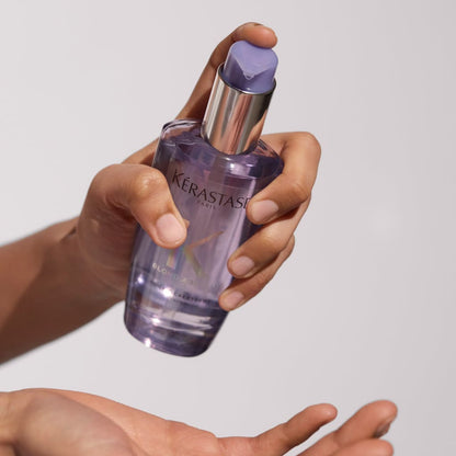 Purple glass bottle of Kérastase Blond Absolut Huile Cicaextreme hair oil held in a hand