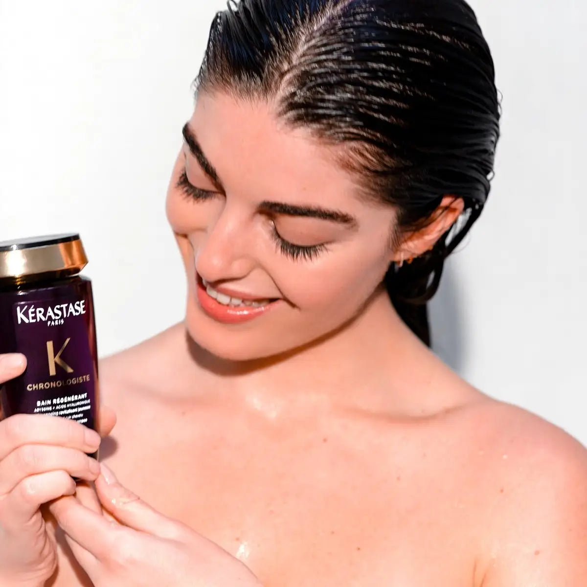 Smiling woman with wet hair holding Kérastase Chronologiste Bain Régénérant Shampoo 250ml